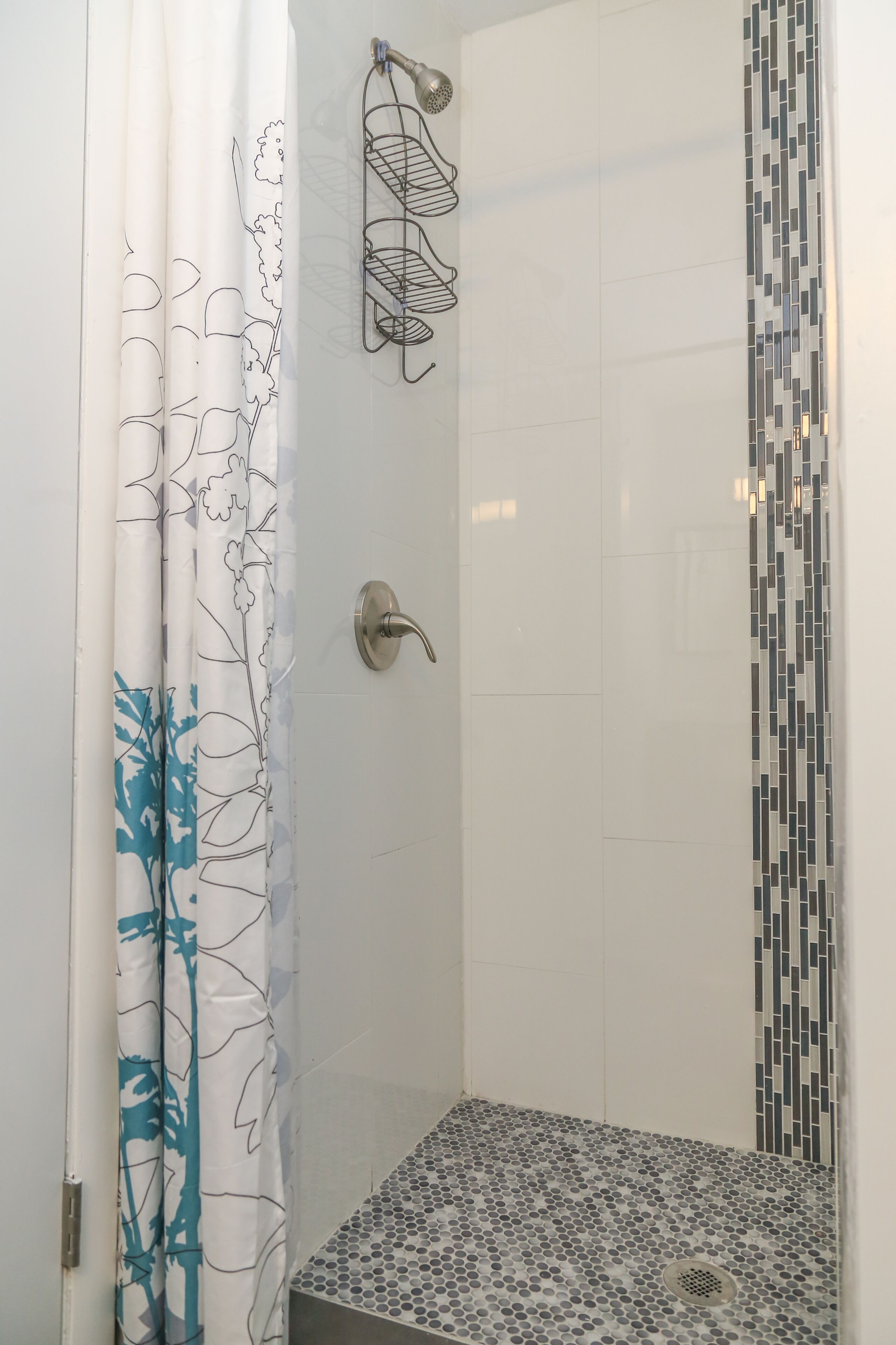 A shower area with a tiled floor, a shower curtain with a floral pattern, and a wall-mounted shower head.