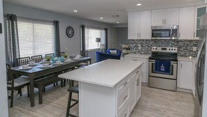 A modern kitchen with white cabinets, a central island, stainless steel appliances, and a dining area with a wooden table and chairs. - Home away from home! (South Pasadena)
