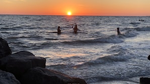 A sunset over the ocean with waves and rocks in the foreground. - Home away from home! (South Pasadena)