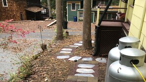 A stone pathway leading to a house with a green exterior and a yellow exterior. There are two large metal tanks on the right side of the pathway. - Butterfly Cottage Close to Everything (Mt Gretna)