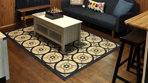 A cozy living room with a wooden ceiling, a ceiling fan, a sofa with decorative pillows, a coffee table, and a patterned rug. - Butterfly Cottage Close to Everything (Mt Gretna)