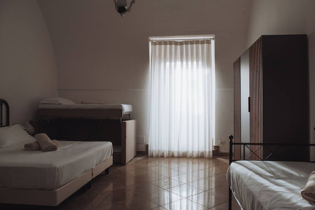 A bedroom with two beds, a wardrobe, and a window with curtains.
