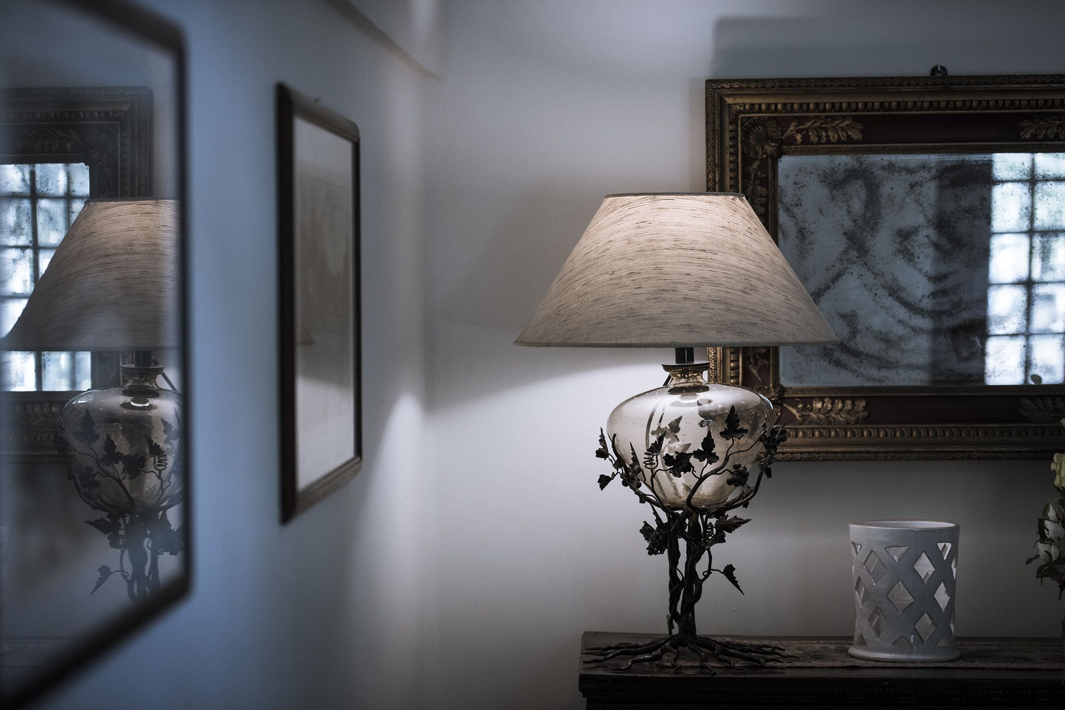 A lamp with a floral design on a table, a framed picture on the wall, and a vase with a lattice design.