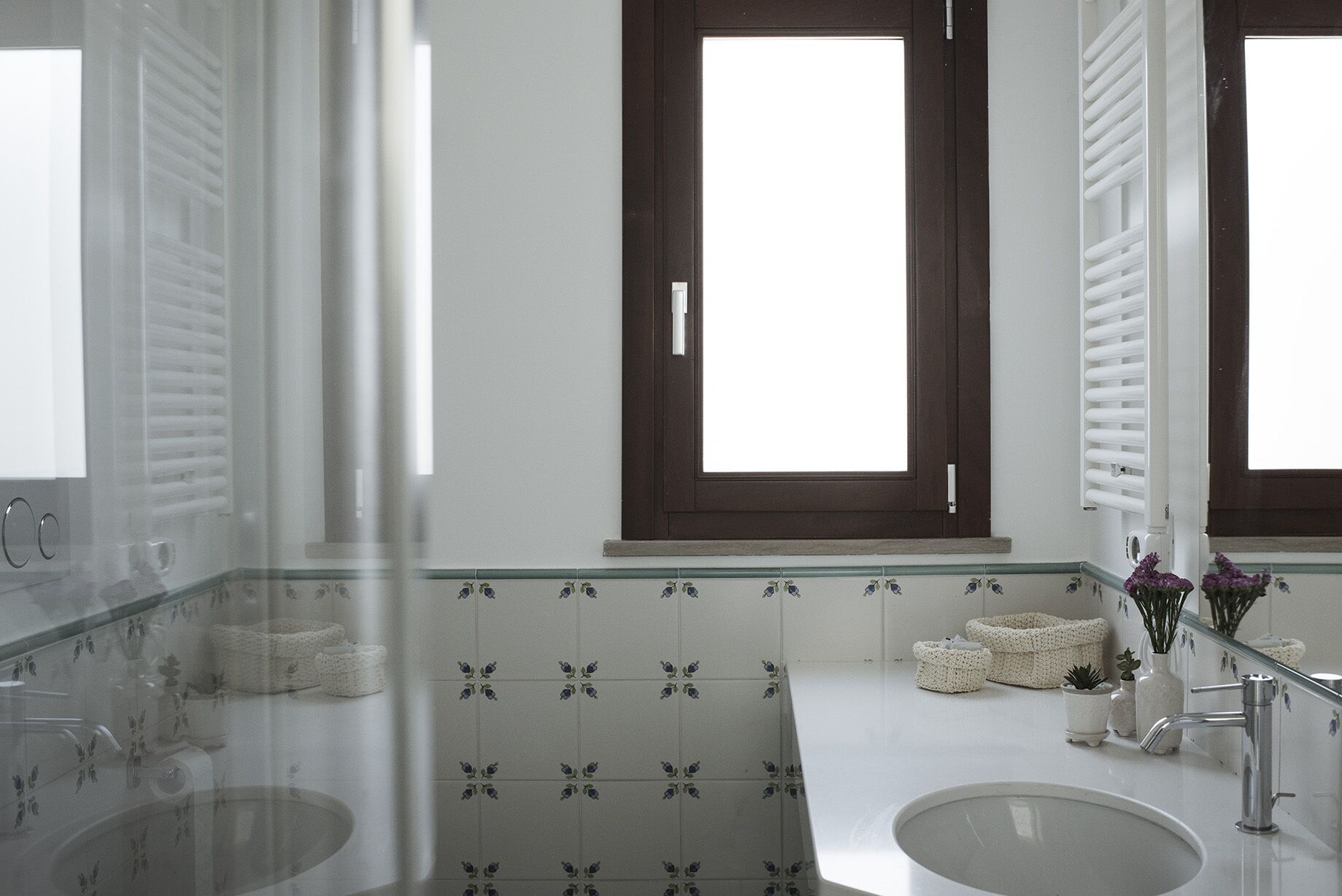 A modern bathroom with two sinks, a glass shower enclosure, and a large window with a dark frame.