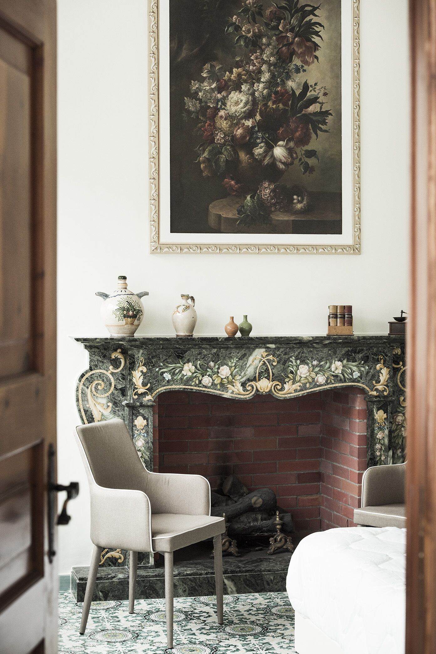 A room with a fireplace, a painting above it, and two chairs.