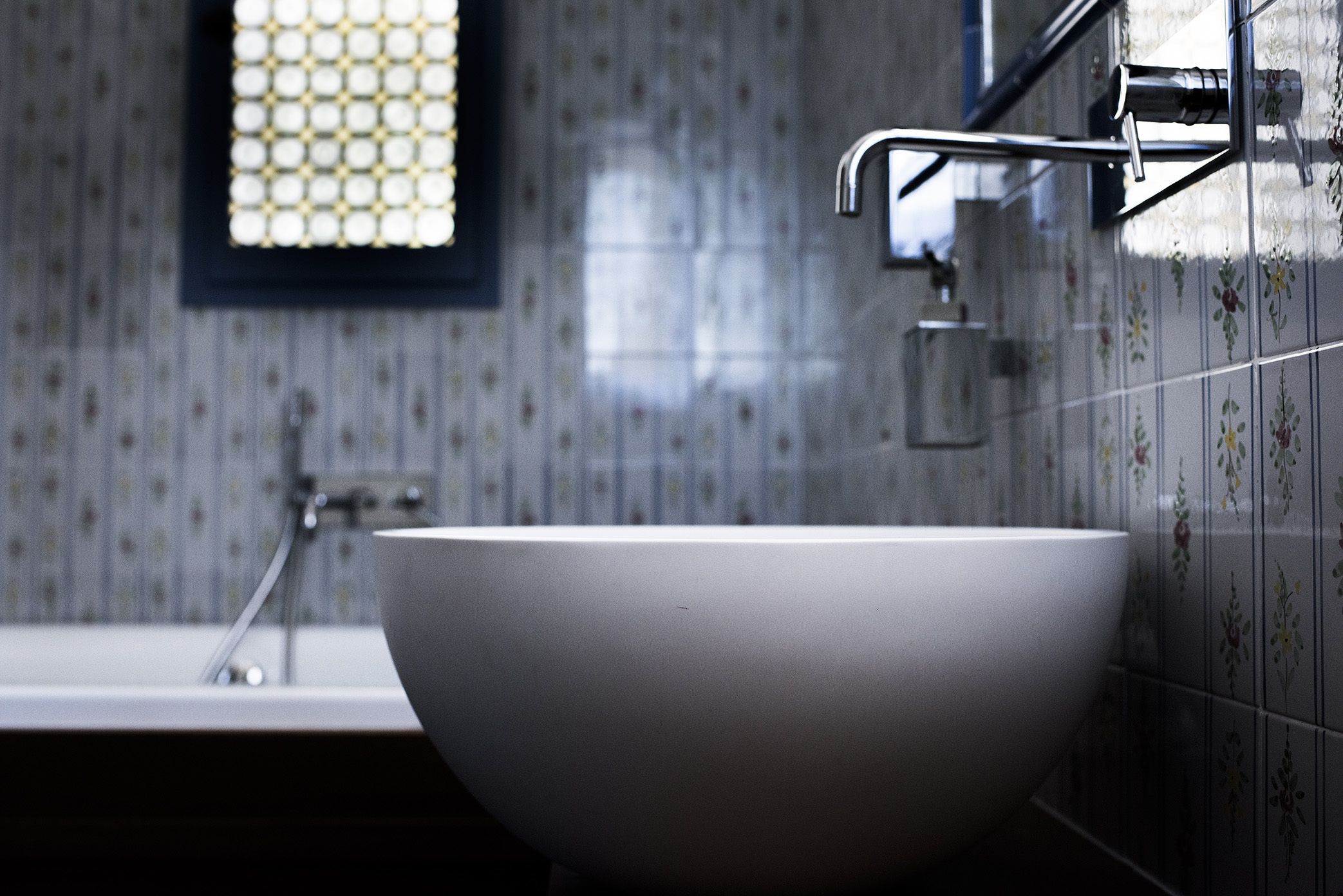 A modern bathroom with a large white sink, a faucet, and a window with a grid pattern.