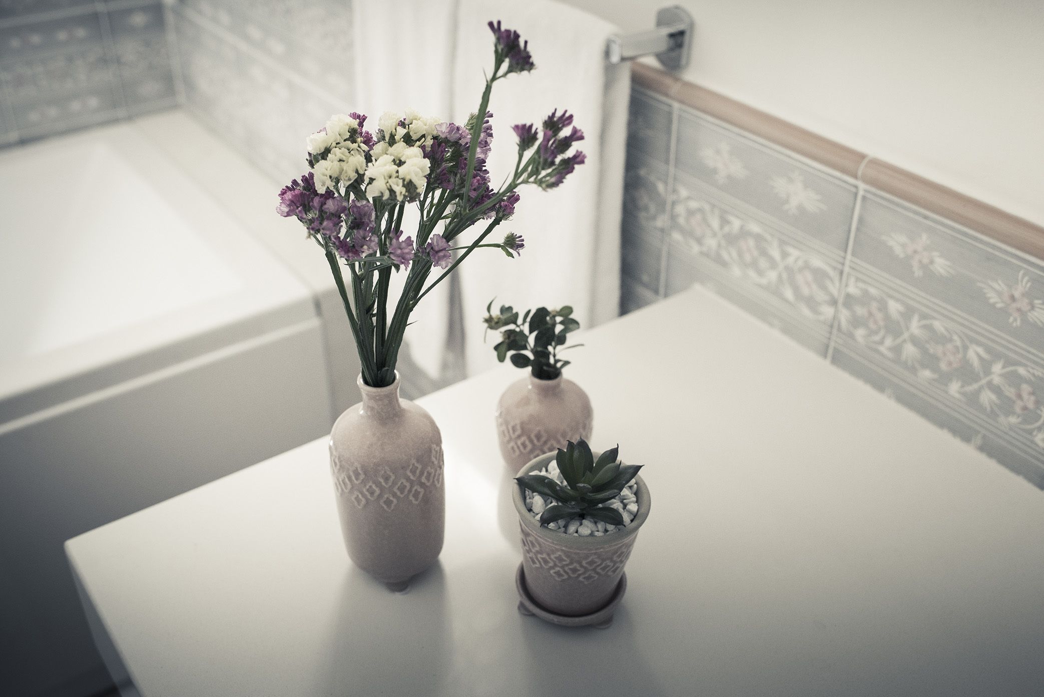 Two vases with flowers and a succulent on a bathroom counter.