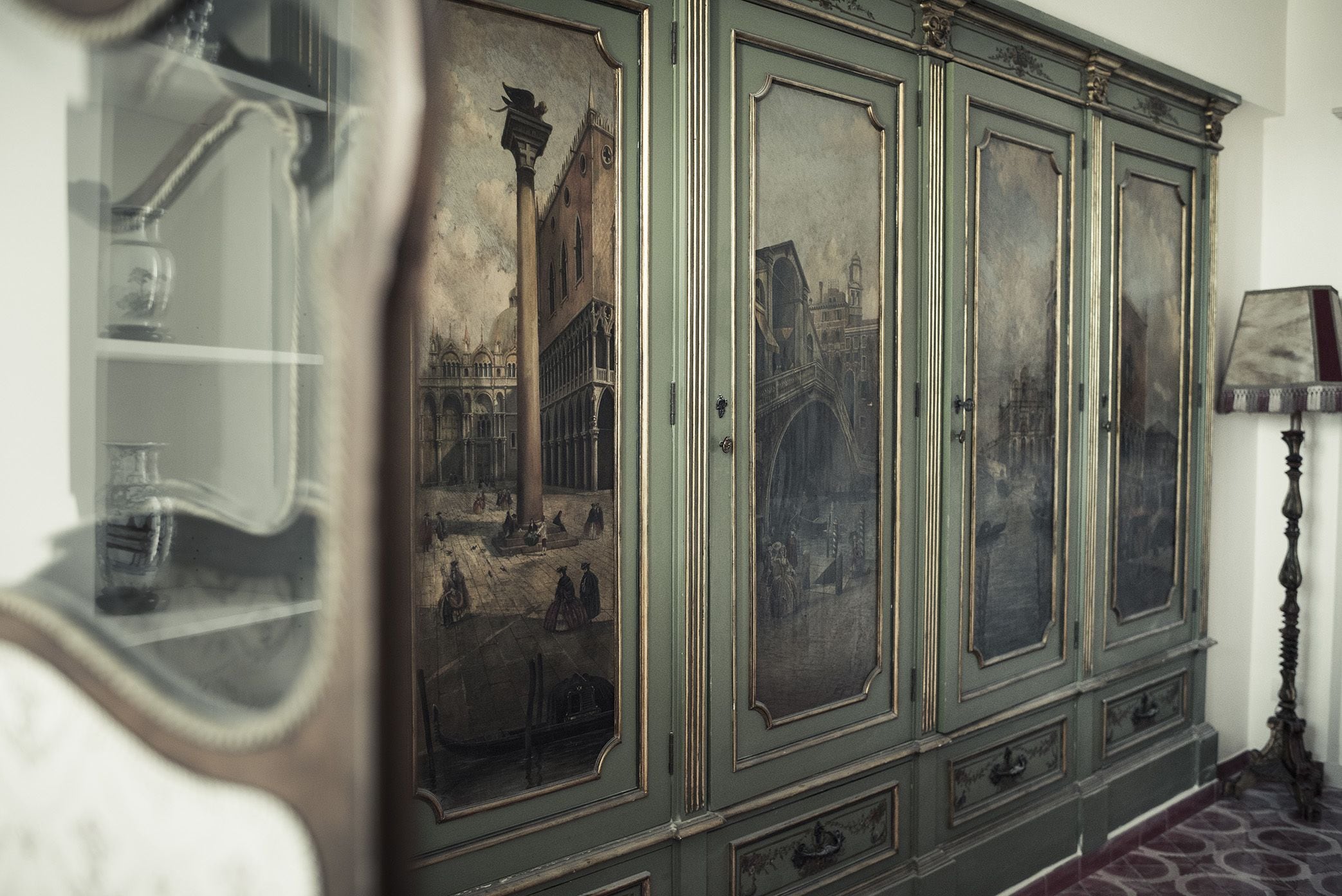 Un mueble verde ornamentado con puertas de cristal, cada una mostrando una escena histórica diferente.