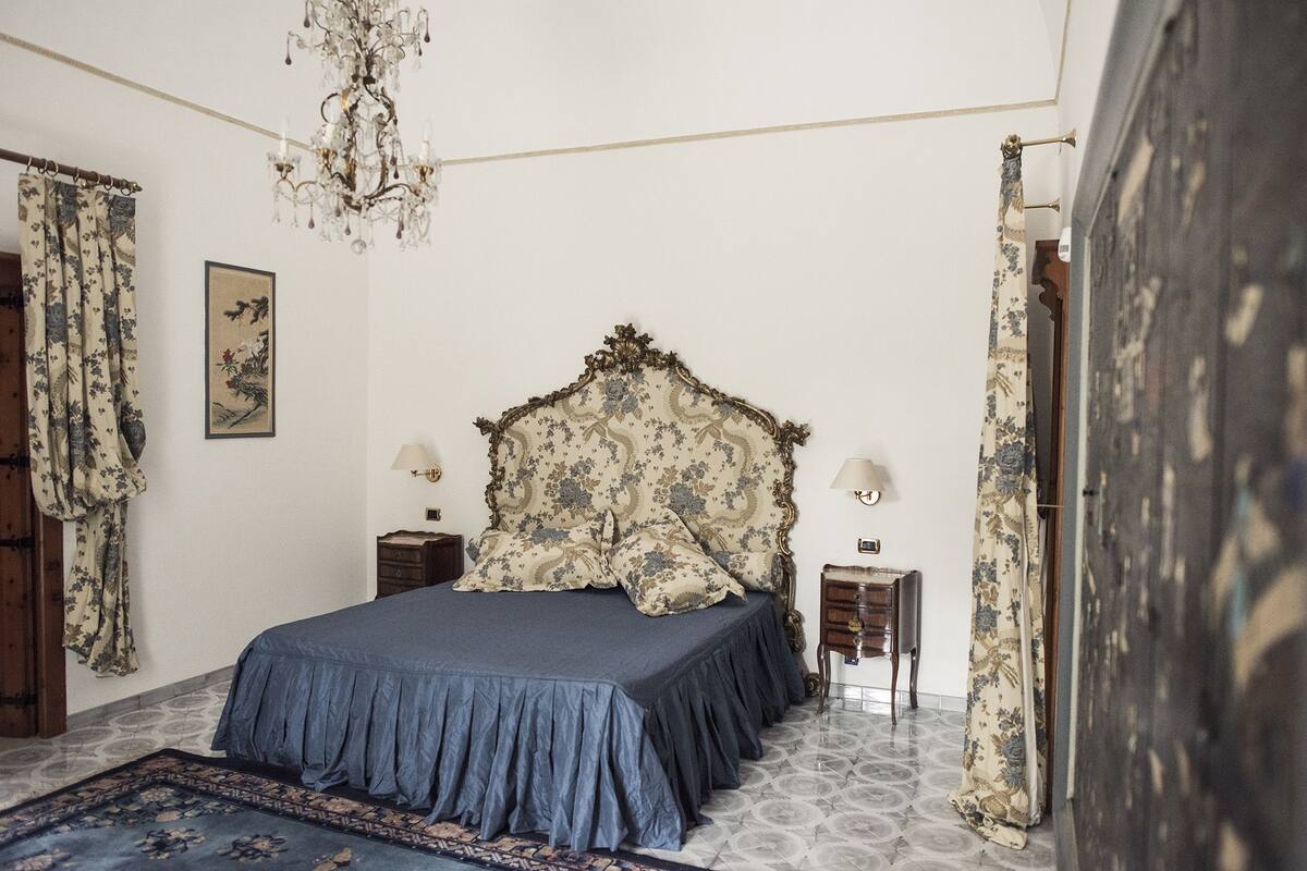 A bedroom with a large bed, two nightstands, a chandelier, and floral curtains.