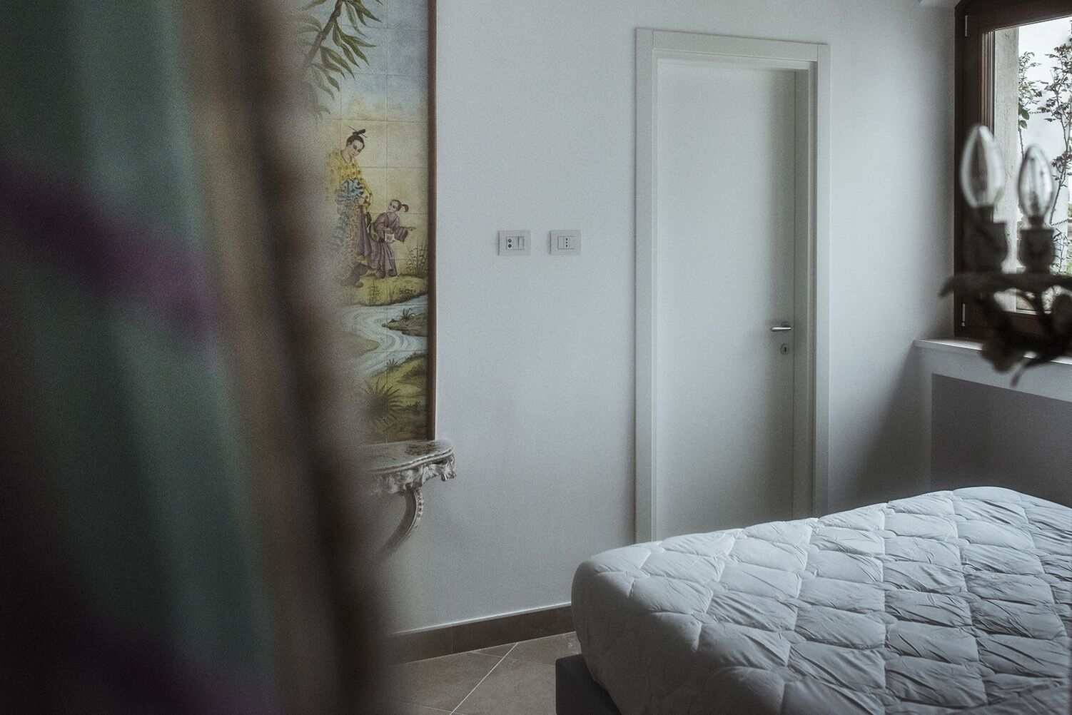 A bedroom with a bed, a door, and a wall-mounted light fixture.