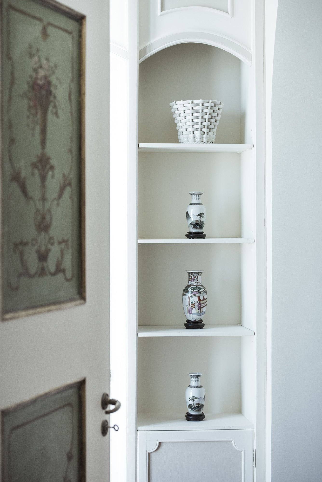Una estantería blanca abierta con jarrones decorativos y una cesta tejida.