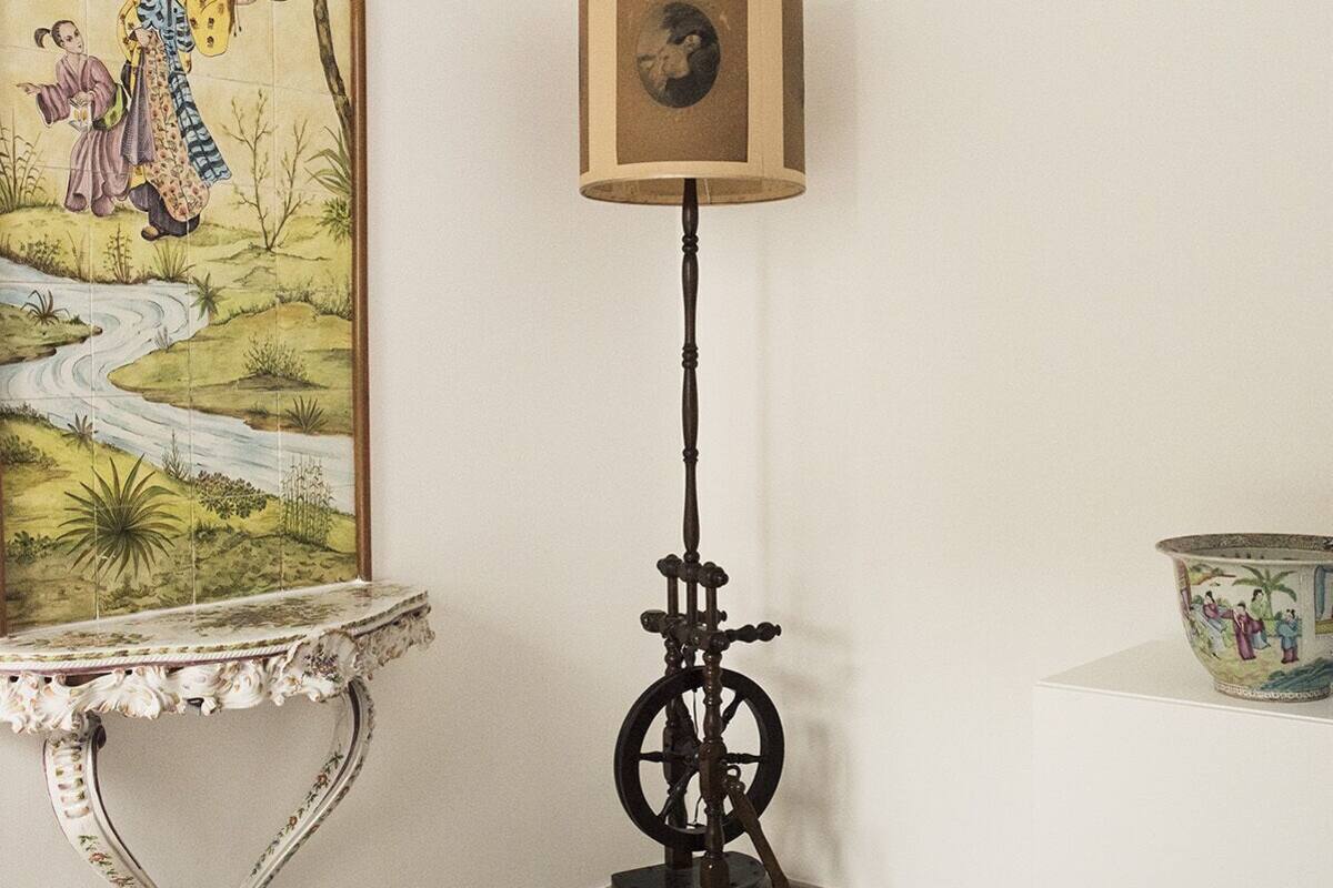 A room with a bed, a table with a painting, a lamp, and a decorative bowl.