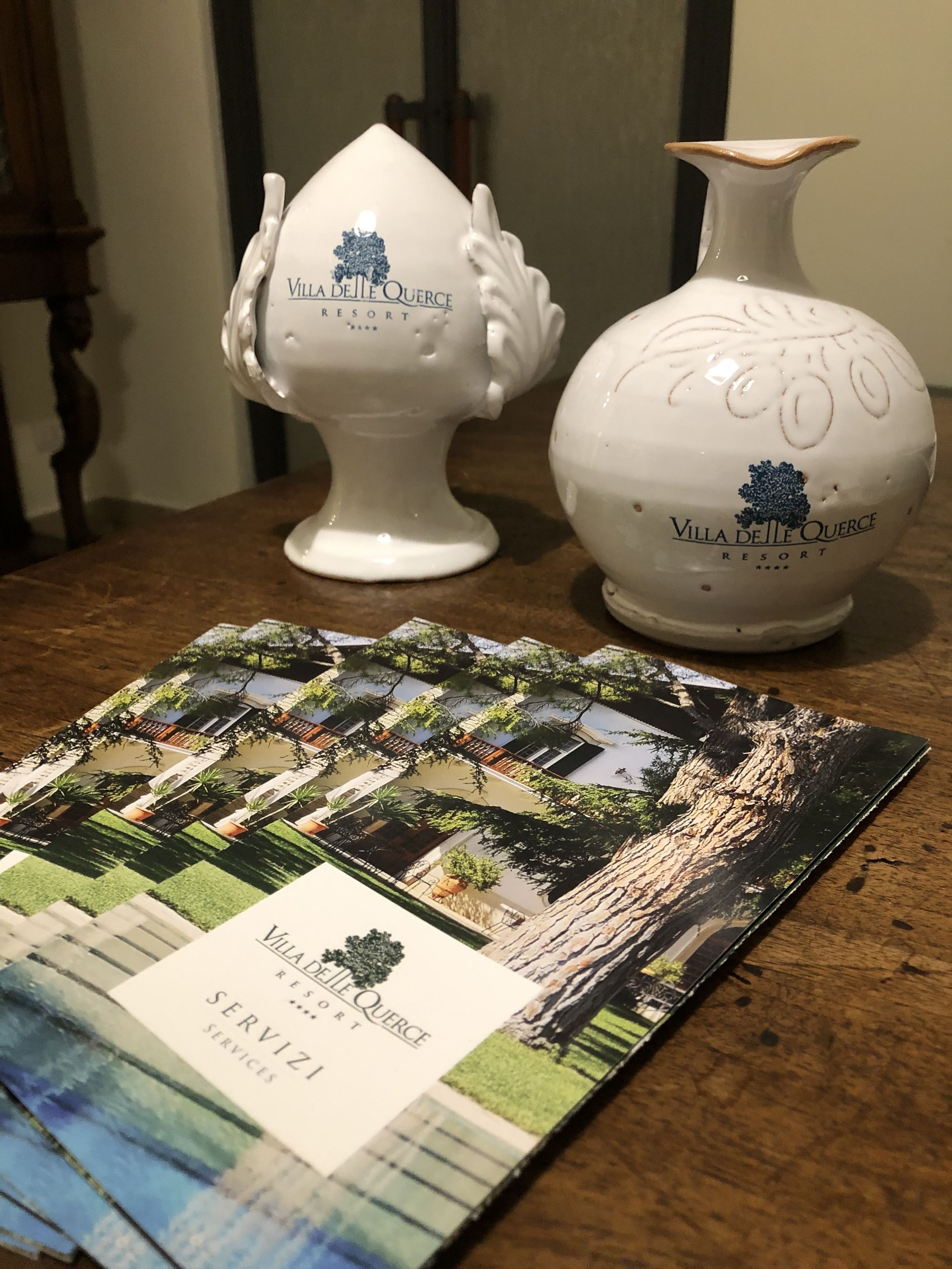 Deux vases en céramique blanche ornés du logo du complexe hôtelier Villa de Le Querce, ainsi qu’une brochure contenant des photos et des textes sur le complexe.