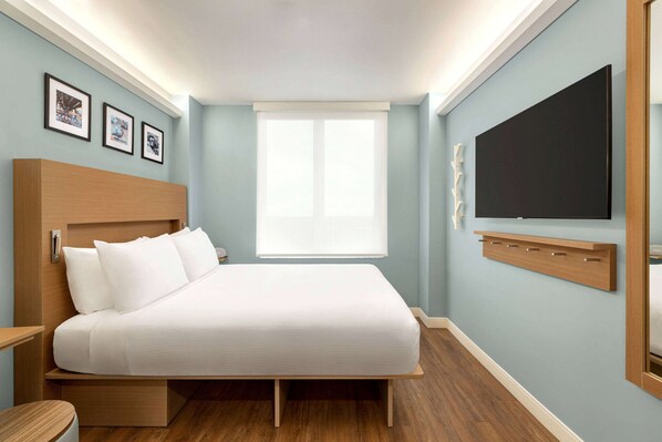 A modern hotel room with a bed, a large window, and a mounted TV.