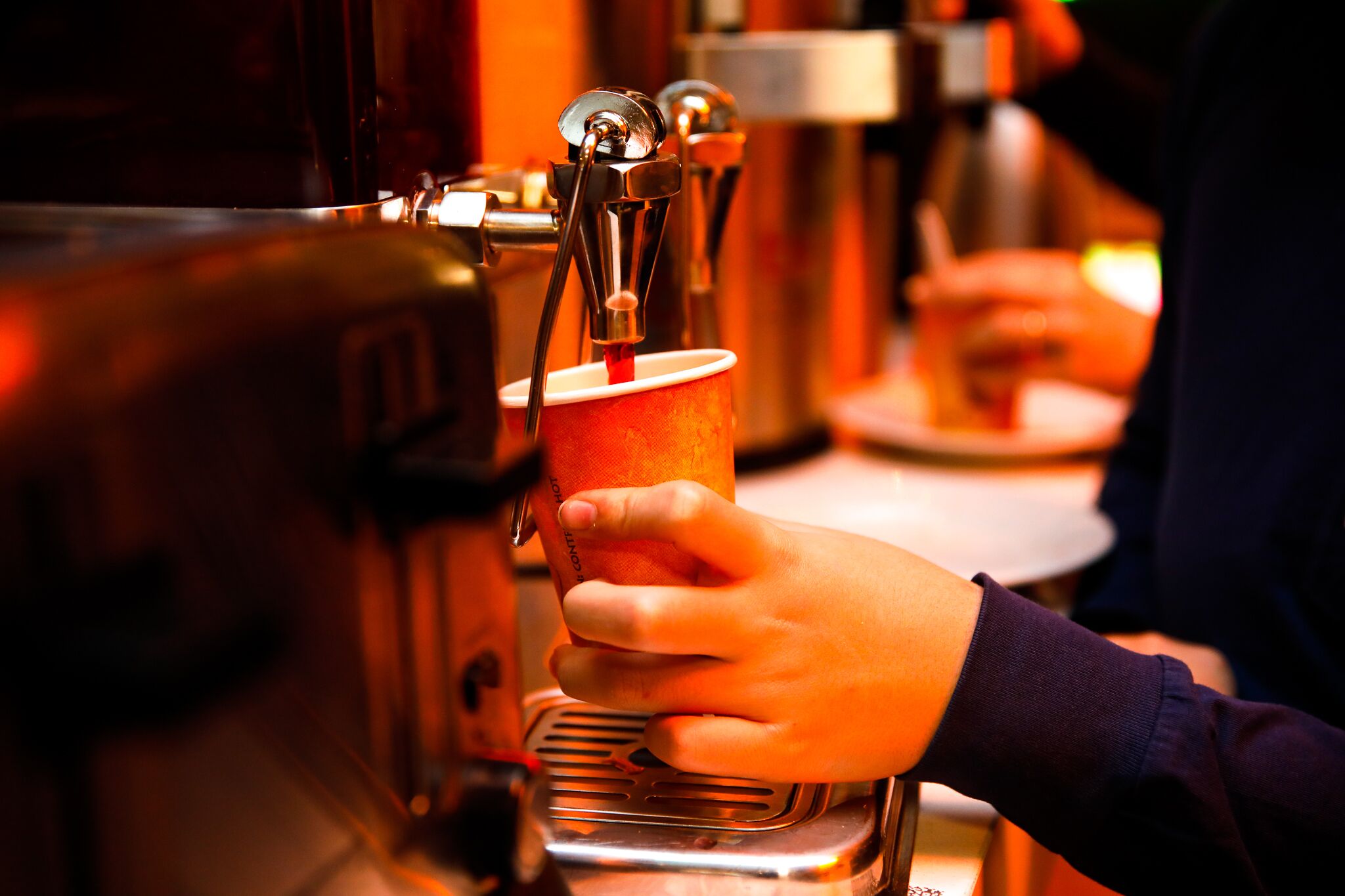 Uma mão segurando uma xícara perto de uma máquina de café.