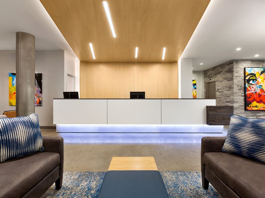 A reception area with a wooden ceiling, a reception desk, two sofas with patterned cushions, and abstract art on the walls.