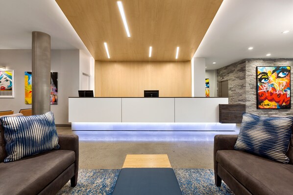 A reception area with a wooden ceiling, a reception desk, two sofas with patterned cushions, and abstract art on the walls. - Wingate by Wyndham Bronx/Haven Park (Bronx)
