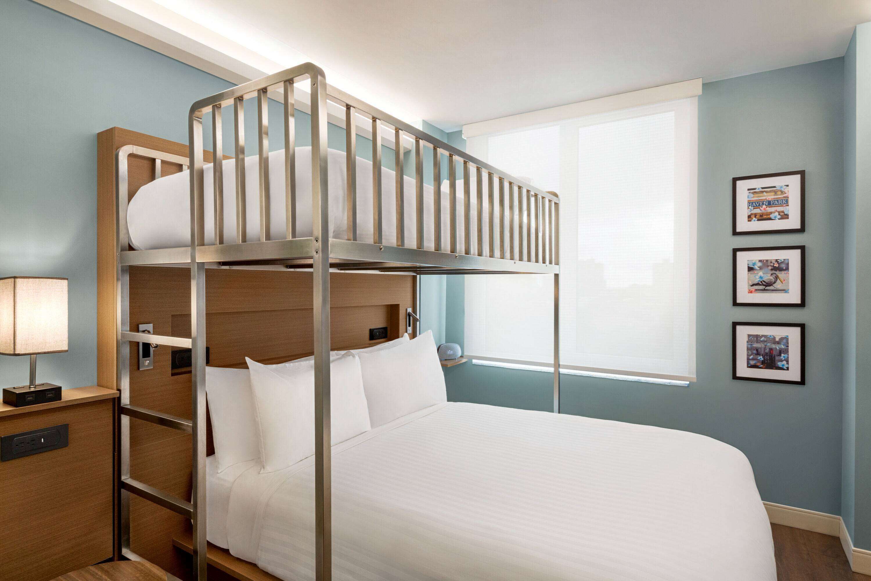 A bunk bed room with a wooden headboard, a bedside table with a lamp, and framed pictures on the wall.