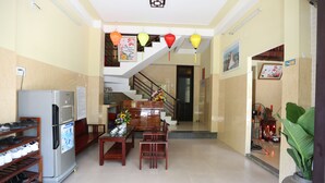 A hotel lobby with a refrigerator, wooden chairs, a table, and a staircase. - Homestay Cuong Thinh (Da Nang)