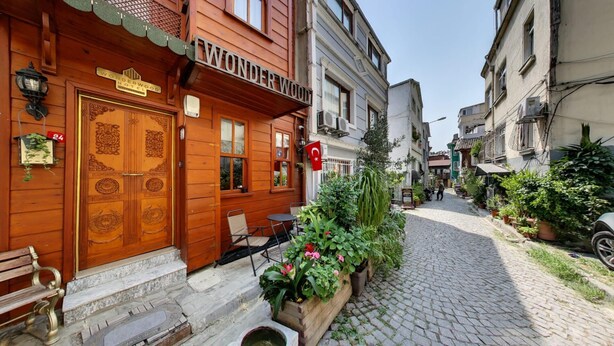 A wooden hotel with a traditional design, featuring a large wooden door with intricate carvings, a small outdoor seating area, and a cobblestone street in the background. - Wonder Wood Hotel (Istanbul)