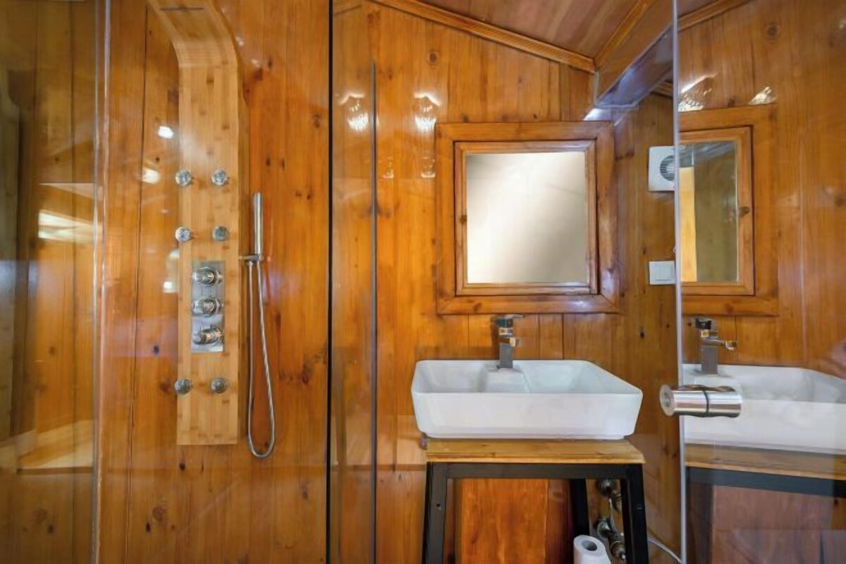 A wooden bathroom with a large mirror, a sink, and a shower with multiple controls.