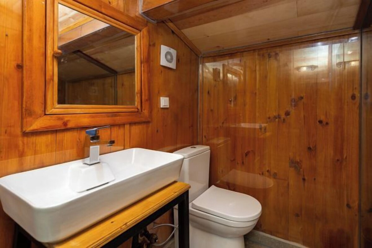 A wooden-paneled bathroom with a white sink, a mirror, and a toilet.
