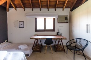 A bedroom with a wooden desk, two chairs, a bed, and a window with a view.