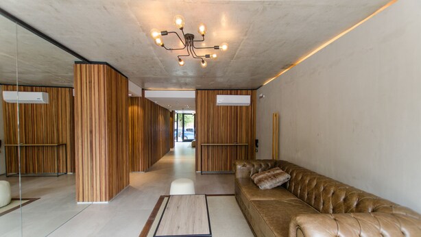 Un hall d’entrée moderne avec un canapé en cuir, un mur décoratif en bois et un luminaire central.