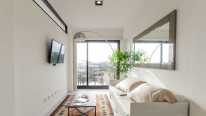 Un salon moderne avec un canapé, une table basse, un téléviseur et une grande fenêtre donnant sur la ville.