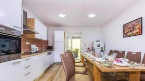 Uma cozinha moderna com armários brancos, bancada de madeira e um espaço de refeições com uma mesa grande para seis pessoas.