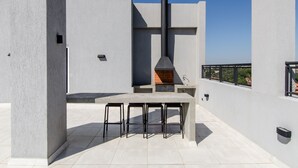 Eine Außenpatio mit Steintisch und Metallhockern, einem eingebauten Grill und einem Schornstein.