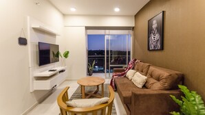 Ein modernes Wohnzimmer mit einem braunen Sofa, einem an einer weißen Wand montierten Fernseher, einem kleinen Holztisch und einem Blumentopf.