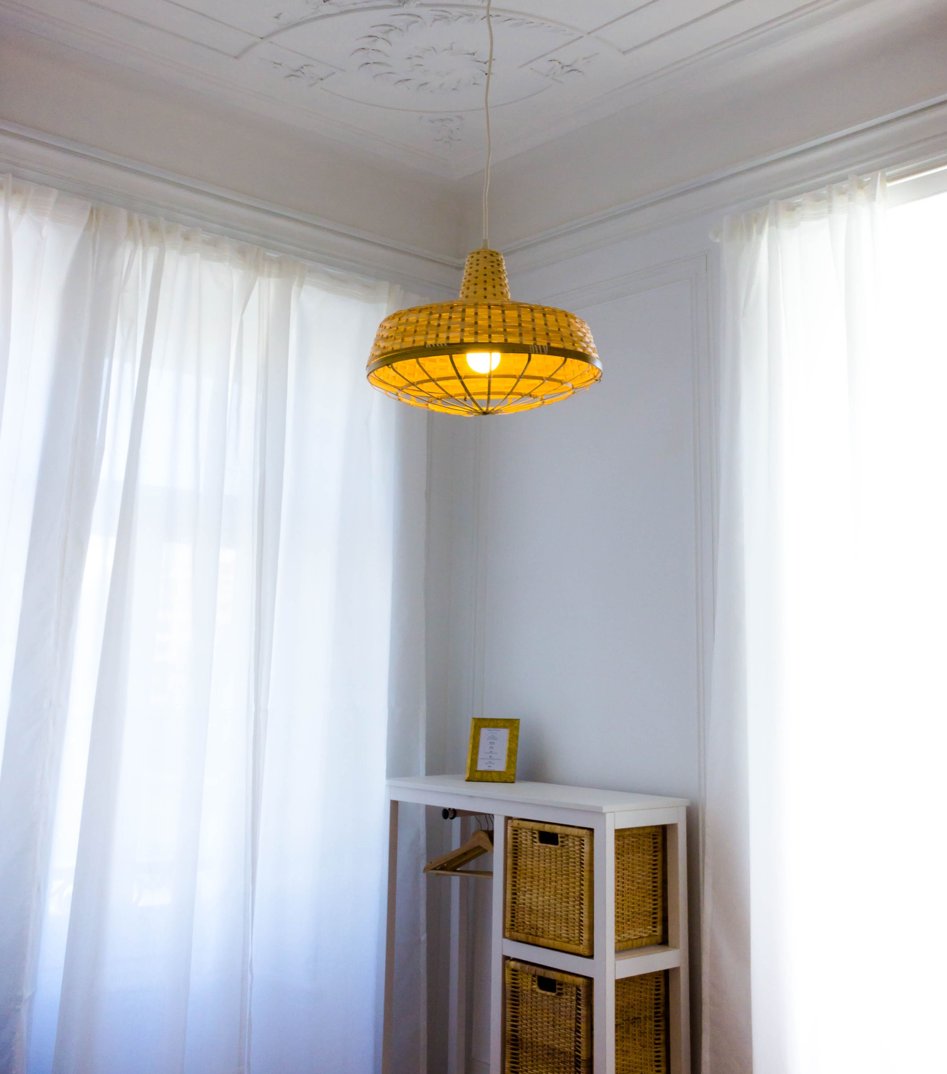 Una habitación con pared blanca, una lámpara colgante amarilla y una consola blanca con cestas.