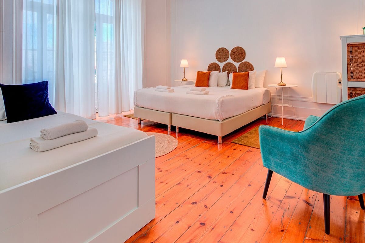 A modern bedroom with a large bed, a sofa, a teal armchair, and a small table with lamps.