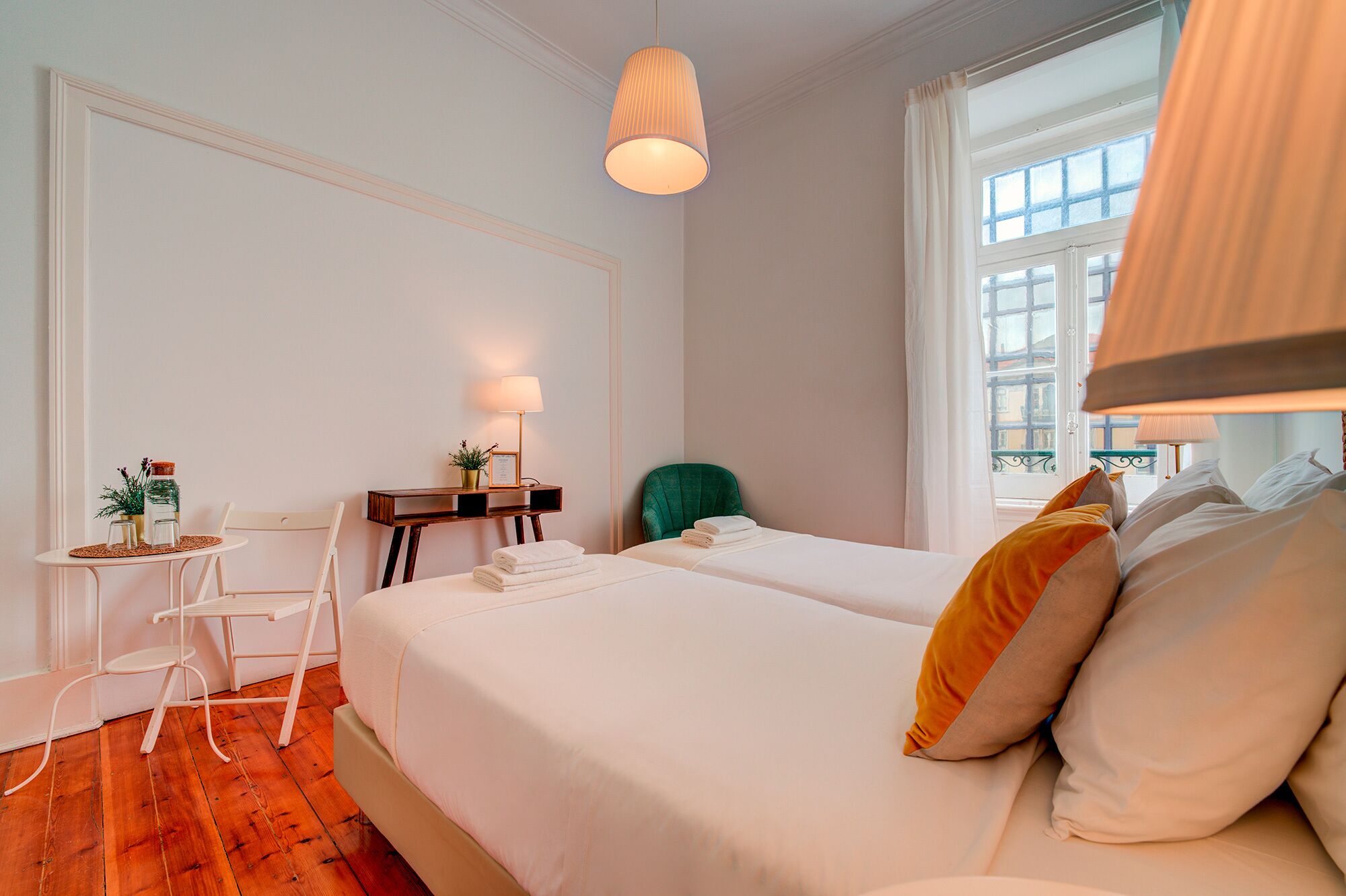 Una habitación de hotel con una cama, un escritorio con lámpara, una silla y una ventana con cortinas.