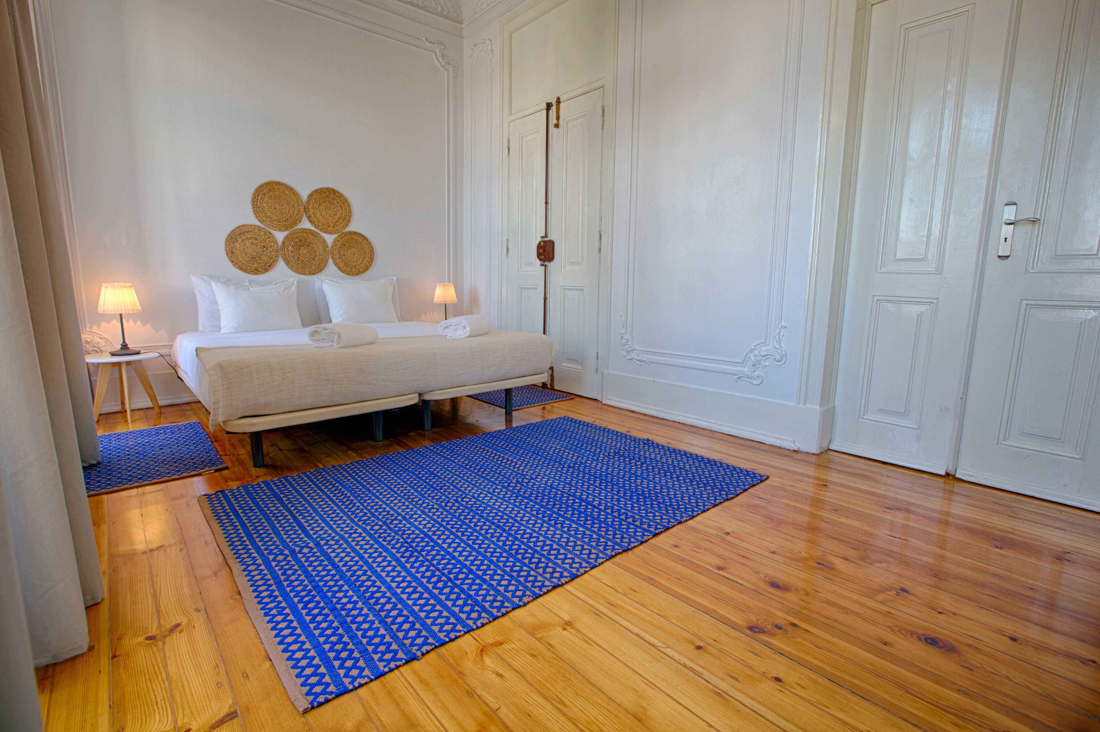 Une chambre à coucher avec un lit, deux tables de chevet, un tapis bleu à motifs et un mur orné d’œuvres d’art circulaires.