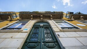 Fachada de edifício com porta dupla verde, número 69, e varanda com grades de metal.