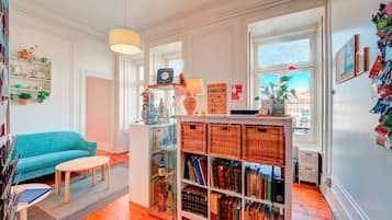 A cozy living room with a teal sofa, a small round table, and a glass display case filled with books and decorative items.