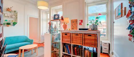 A cozy living room with a teal sofa, a small round table, and a glass display case filled with books and decorative items.