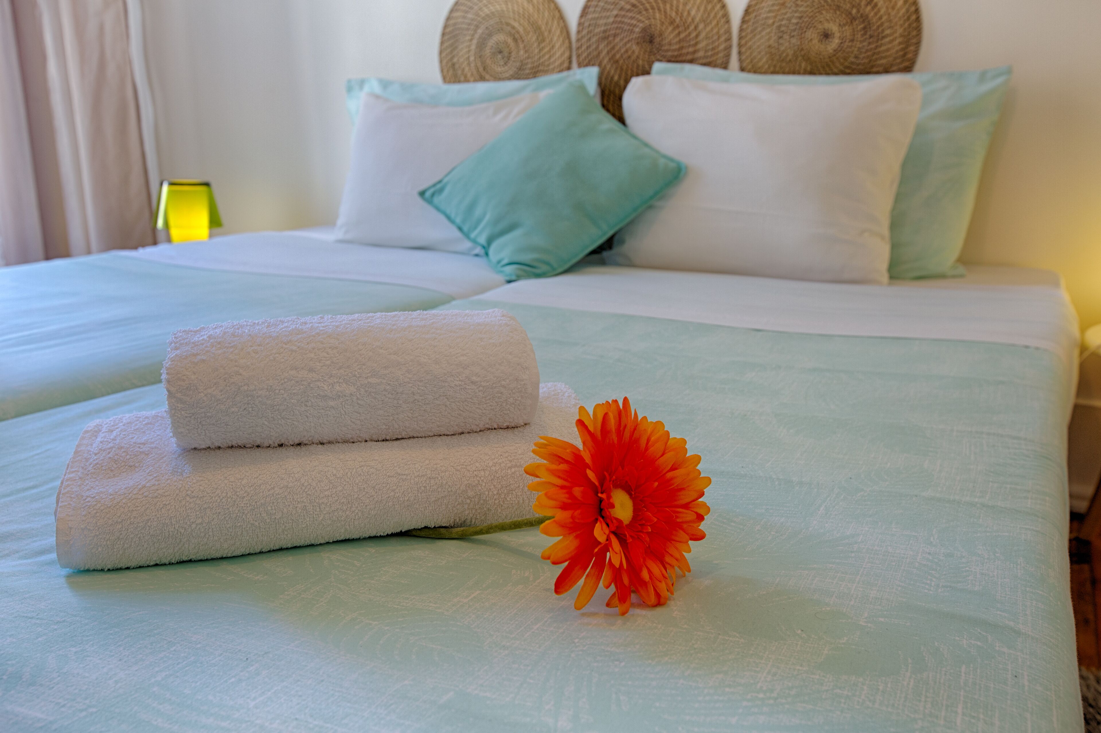 A neatly made bed with white linens and a single orange flower.