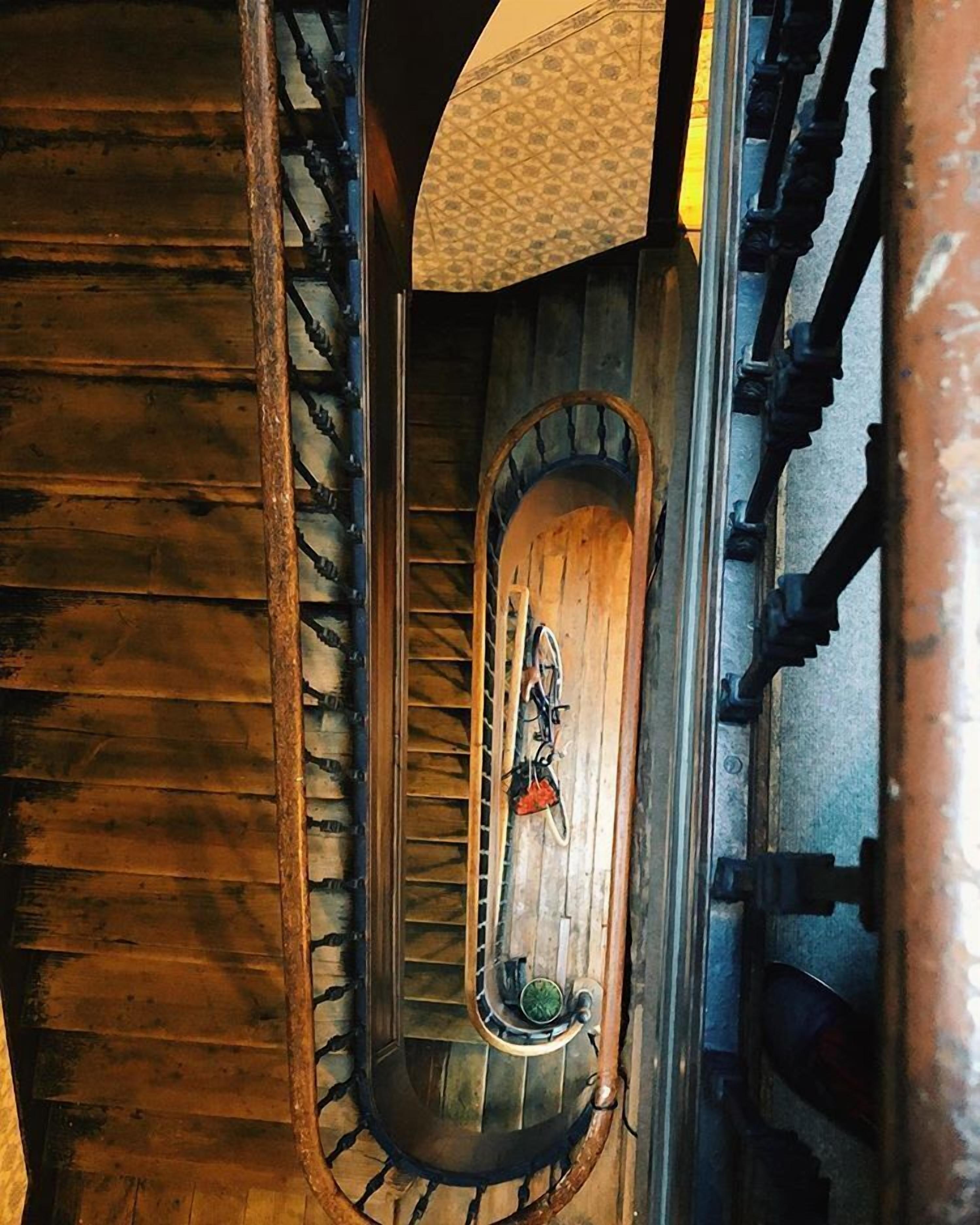 A spiral staircase with wooden steps and metal railings, leading to a landing area with a bicycle and a small table.