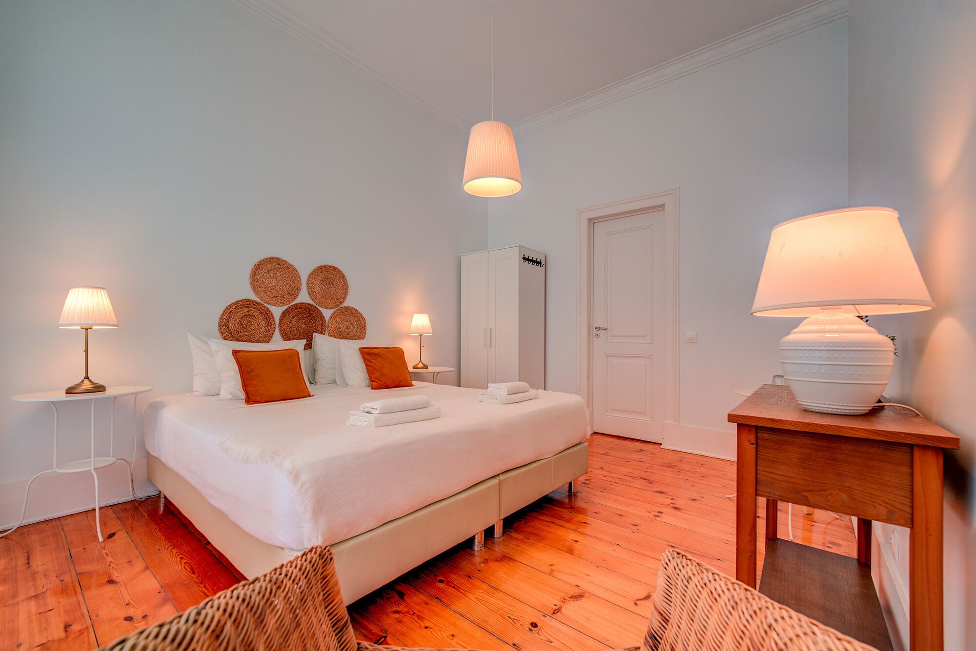 A neatly arranged bedroom with a bed, two bedside tables with lamps, a wardrobe, and a door.