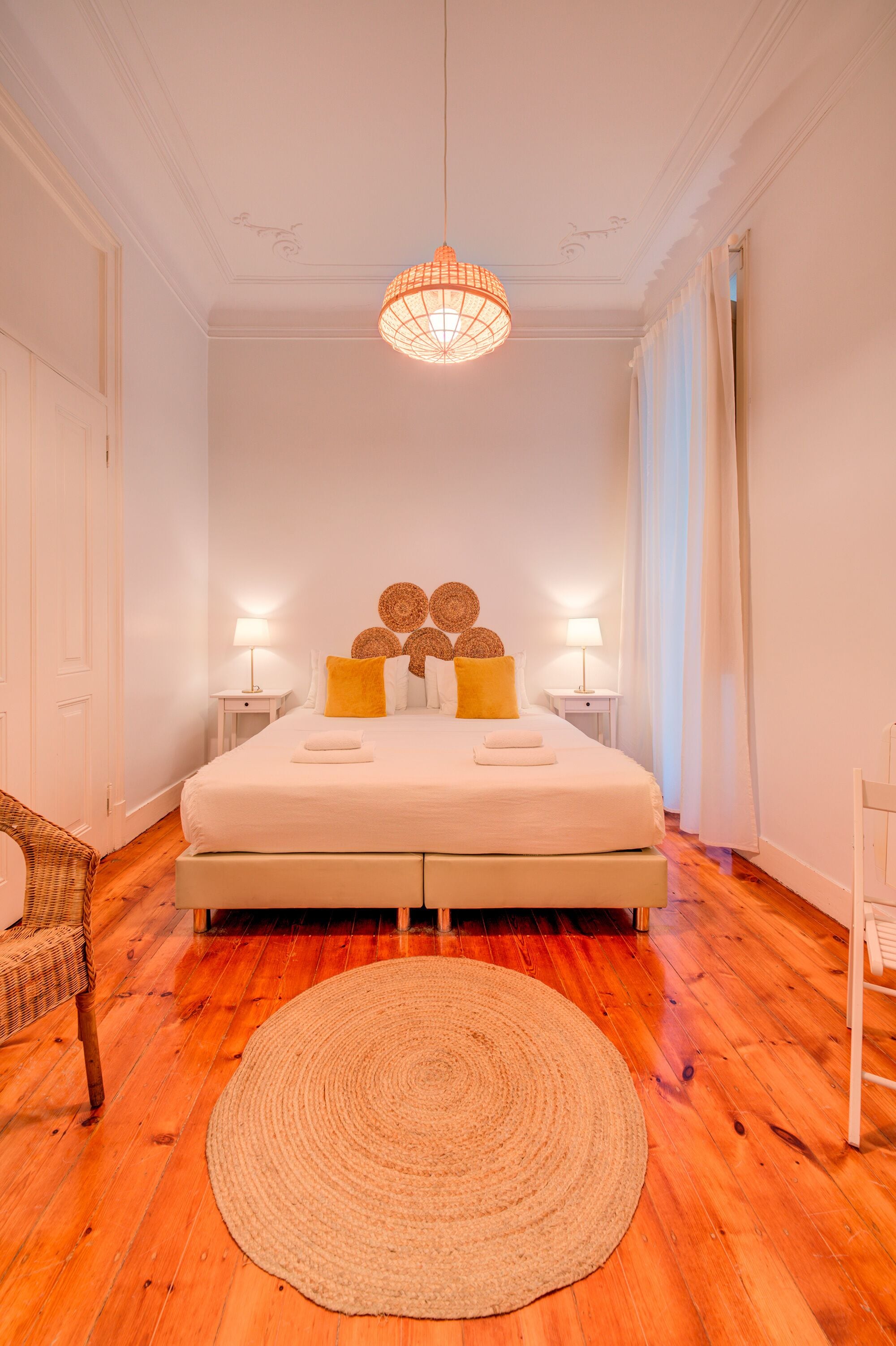 A bedroom with a large bed, two bedside tables, a woven rug, and a hanging light fixture.