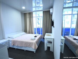 Relax in this serene hotel room featuring a large bed, a compact desk, and large windows with curtains.