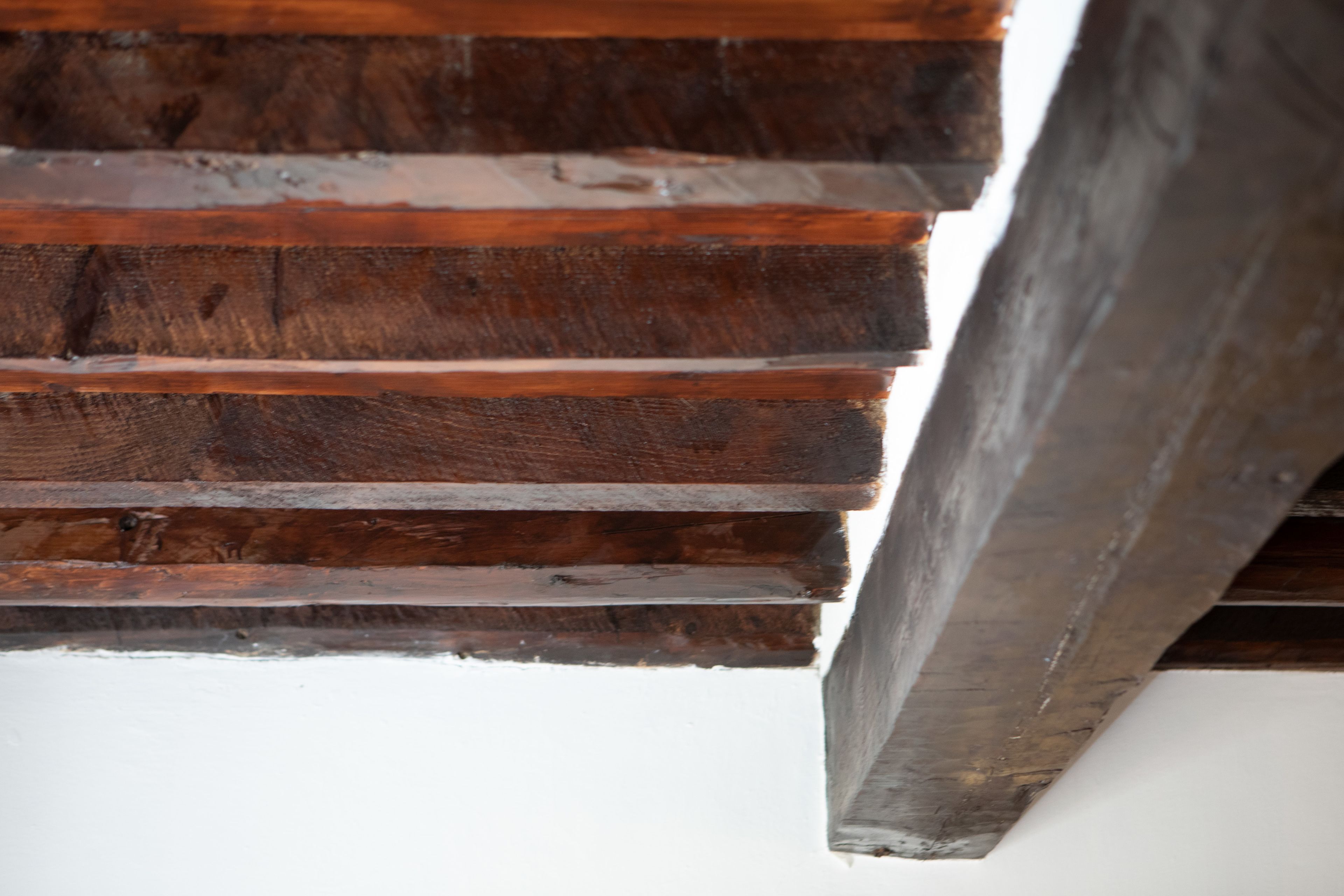 Ein Detailaufnahme einer Holztreppe mit einer weißen Wand unten.