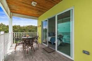 Ein überdachter Balkon mit Tisch und Stühlen, eine Glastür zum Schlafzimmer und Blick ins Grüne.