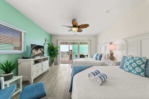A bedroom with a bed, a desk, a chair, a ceiling fan, and a balcony with a view.