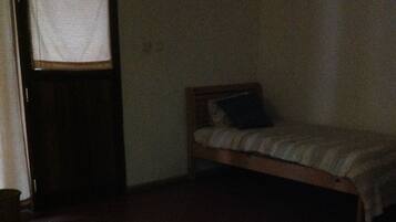 A dimly lit room with a single bed, a window with a blind, and a patterned rug on the floor.