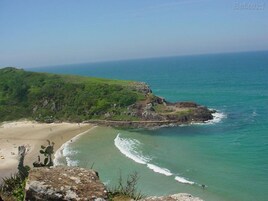 Un paisaje costero con una playa arenosa, aguas turquesas cristalinas y colinas verdes.