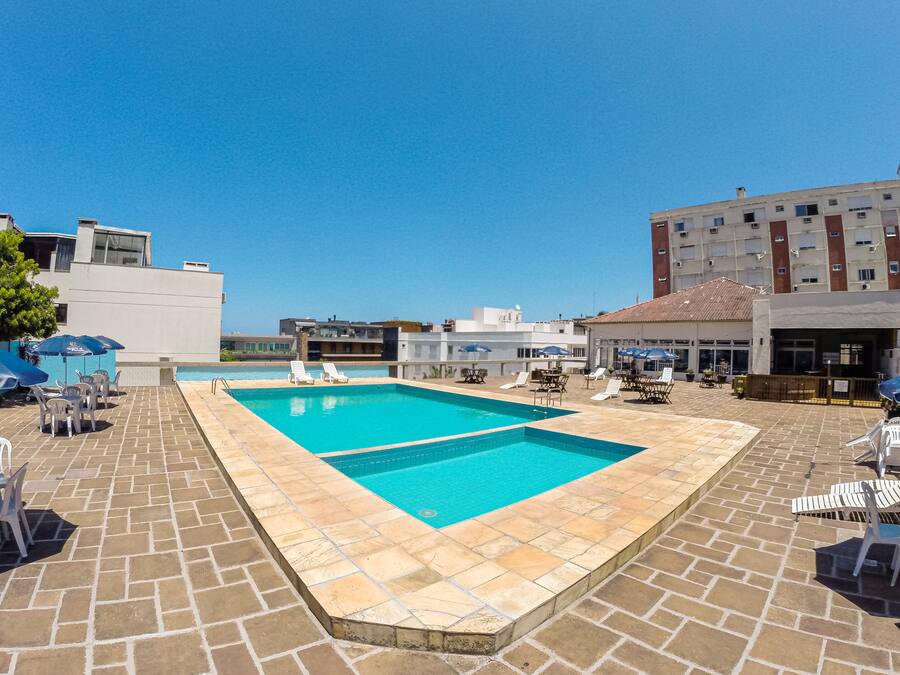 Una piscina rectangular con agua cristalina azul, rodeada de baldosas de piedra. Hay sillas de descanso y sombrillas alrededor de la piscina.